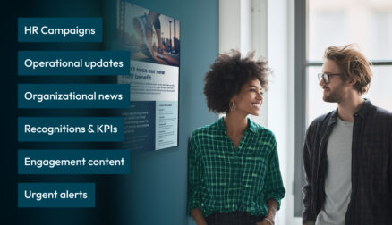 Two coworkers chatting next to a digital signage screen on a blue wall.